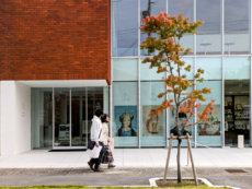 一級建築士事務所・株式会社ディーディーティー（d/dt Arch.）設計の軽井沢安東美術館の前を通る男女と、紅葉した街路樹